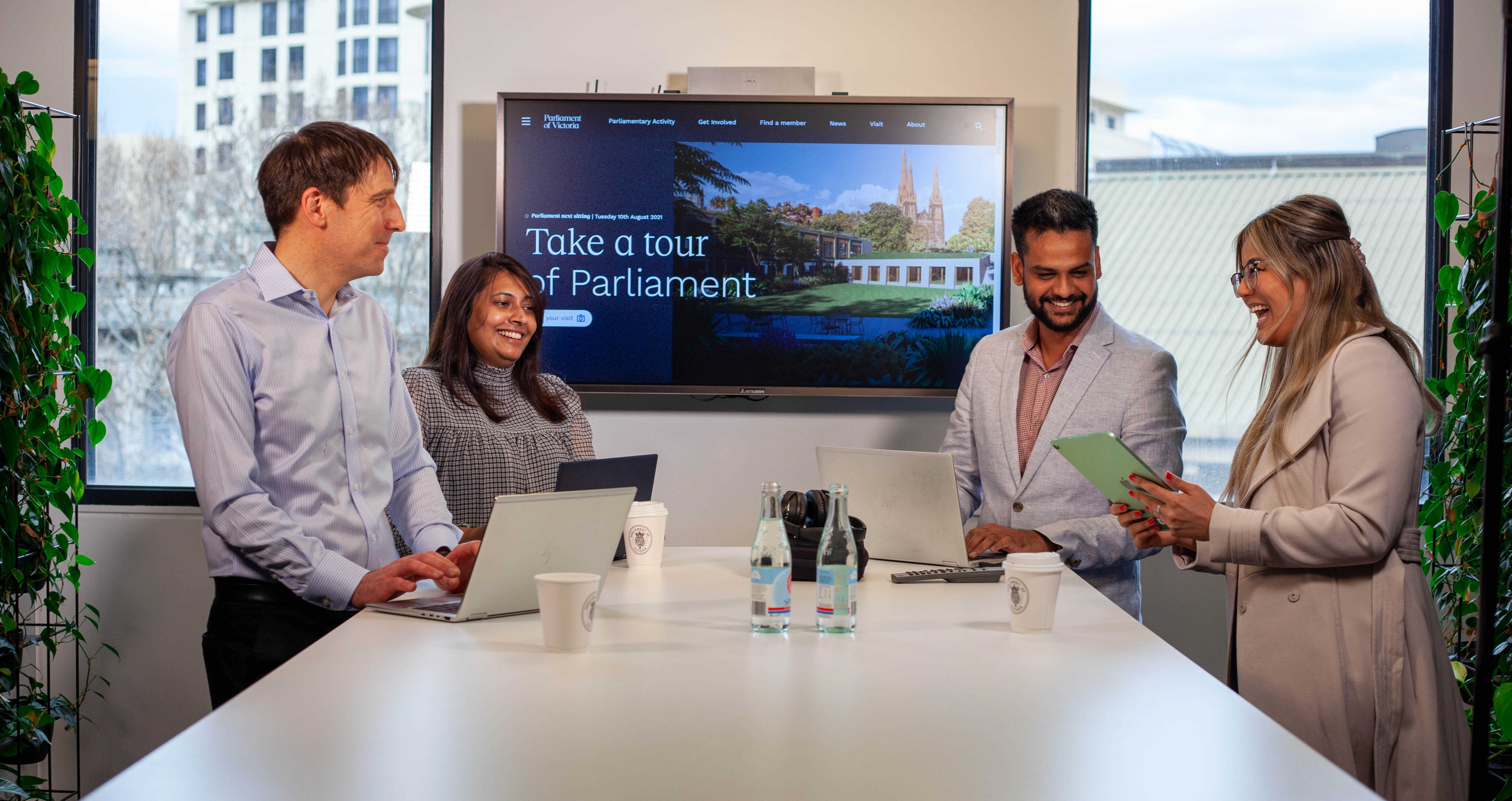 Four Parliament employees meet with a screen in the background with an image of Parliament 