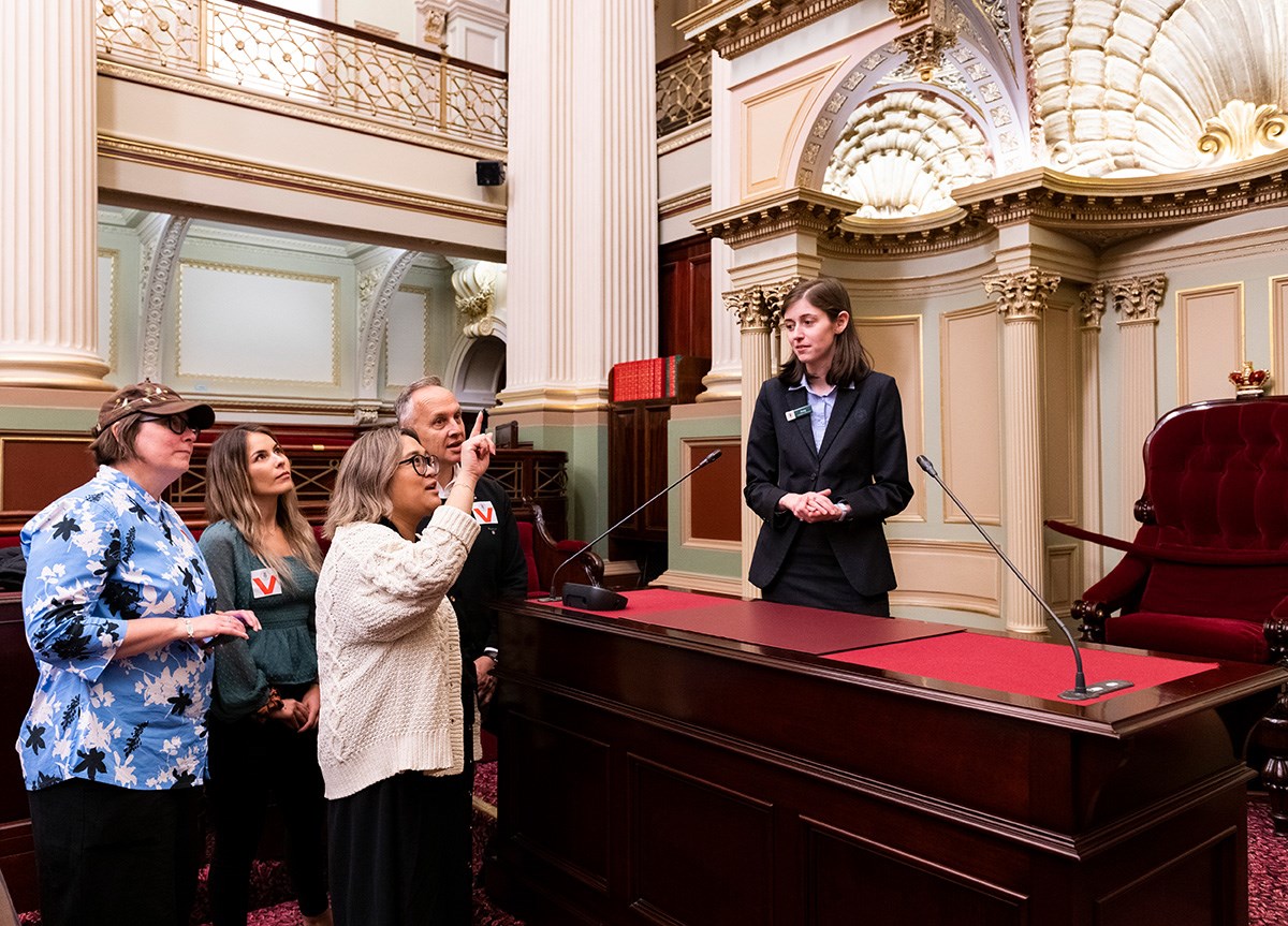 A visitor points up at a feature of the Legislative Assembly chamber.