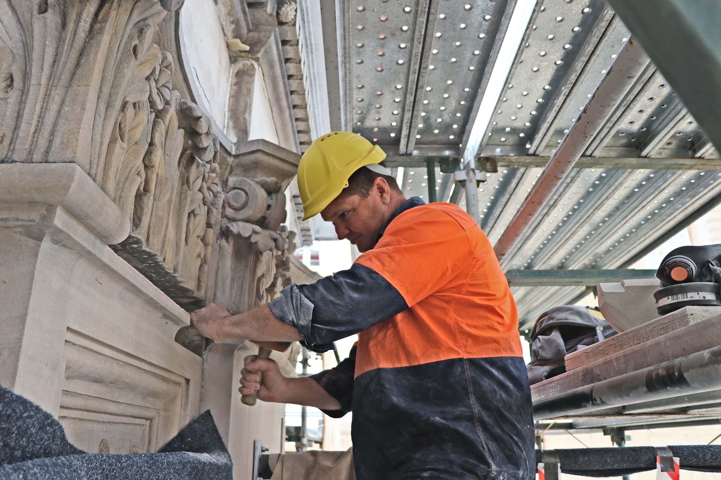 Glenn Torbet, stonemason, stands amongst scaffolding as he works on the stonework of Parliament House.
