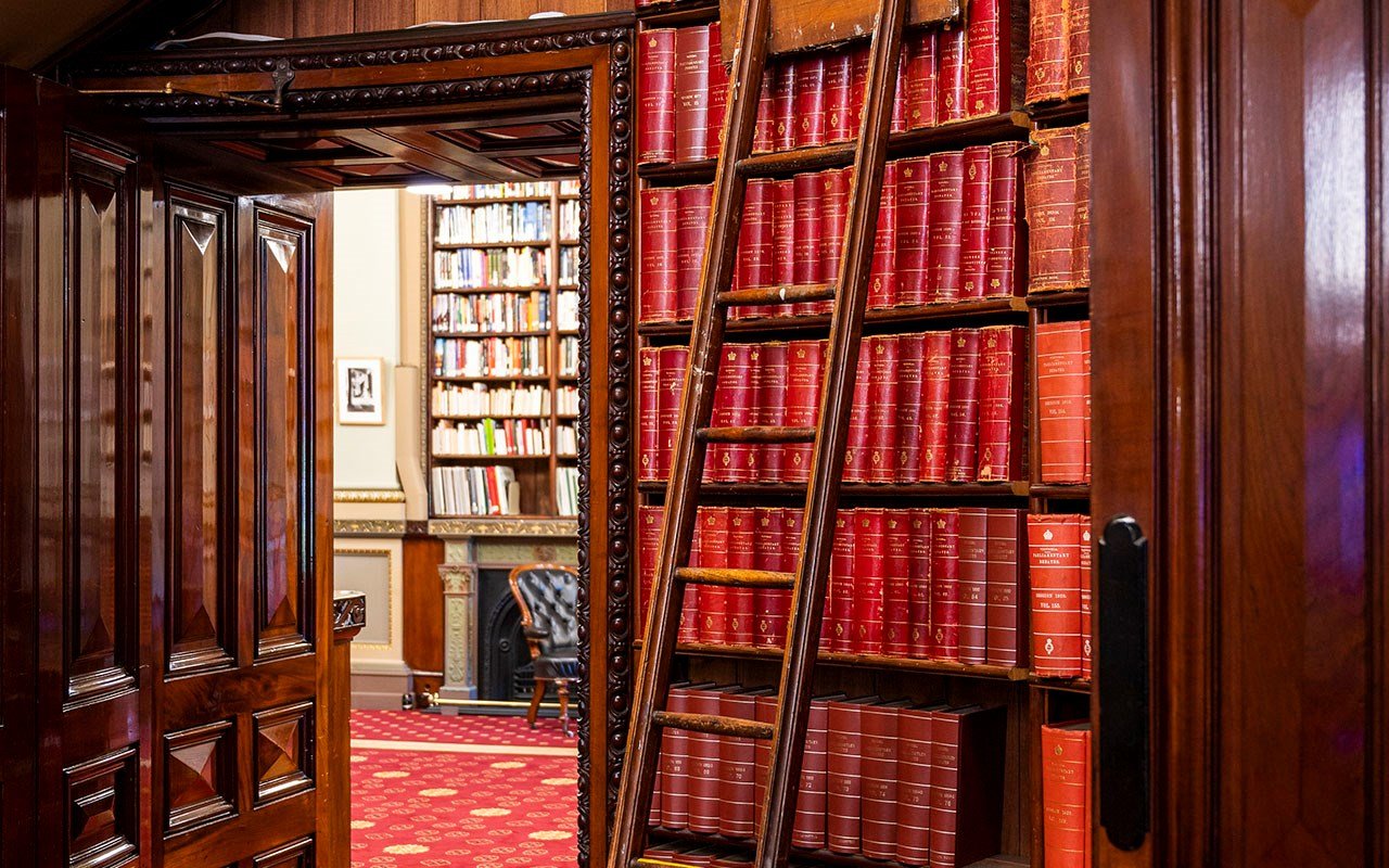 A ladder leaning over a shelf full of red leather-bound books in a library