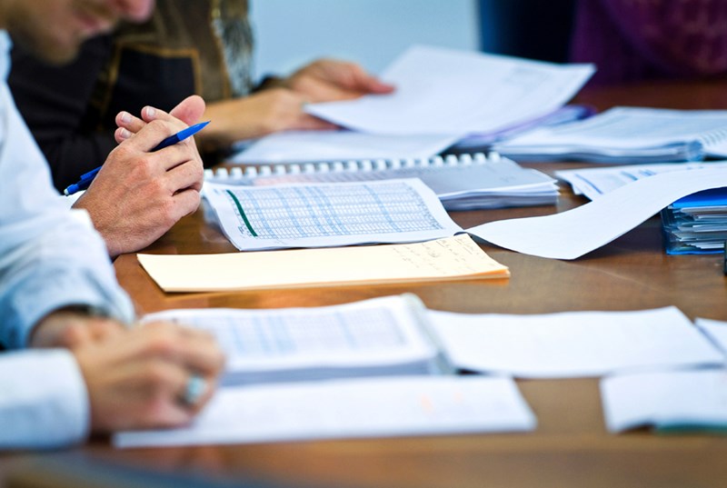 A group of three people make notes on spreadsheets and notebooks